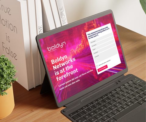 Photo of a tablet on a desk displaying a Boldyn Networks webpage with bold pink and orange digital graphics, headline text reading ‘Boldyn Networks is at the forefront,’ and a contact form alongside.