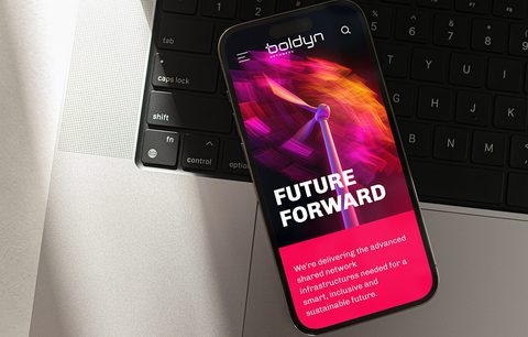 Photo of a smartphone resting on a laptop keyboard, displaying the Boldyn Networks ‘Future Forward’ campaign screen with a wind turbine graphic and bright digital colors, emphasizing innovation and forward-looking technology.