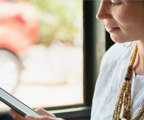 Close-up photo of a person holding an e-reader near a window, softly lit by natural light, conveying the ease, focus, and portability of digital reading.